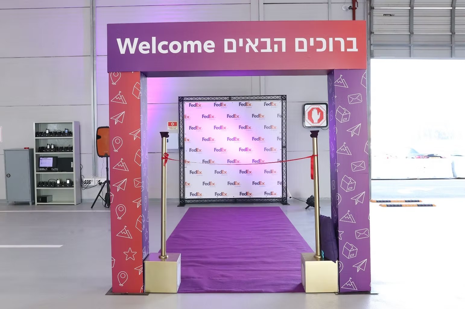שער הכניסה לאירוע: מבנה שער עם הכיתוב ברוכים הבאים, שטיח סגול וקיר צילום ברקע